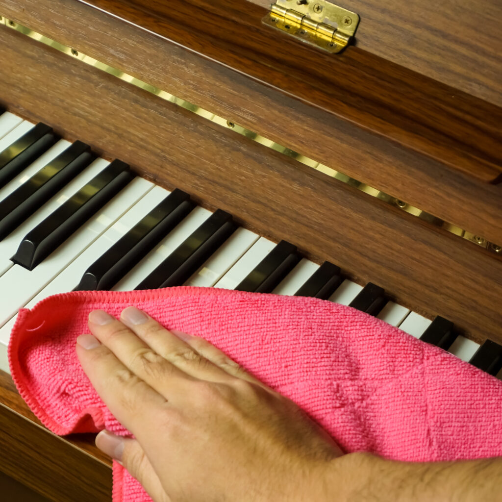Nettoyer son piano: Entretien facile du clavier et du bois Main nettoyant les touches blanches et noires d'un piano en bois avec un chiffon microfibre rose. Détails en laiton visibles.