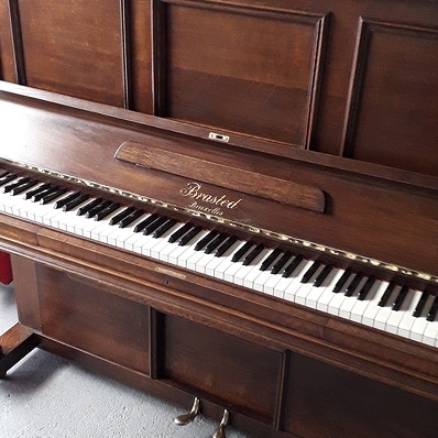 Brasted Bruxelles : Piano droit vintage en bois Piano droit Brasted Bruxelles en bois sombre, avec clavier complet noir et blanc et deux pédales en laiton. Aspect vintage.