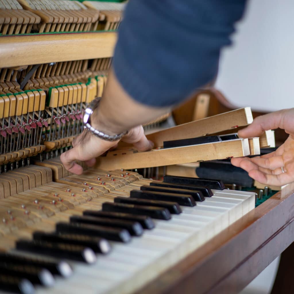 Réparation piano: Mécanisme interne, touches et action Mains ajustant le mécanisme interne d'un piano ouvert. Marteau, étouffoirs et touches visibles pendant la réparation.